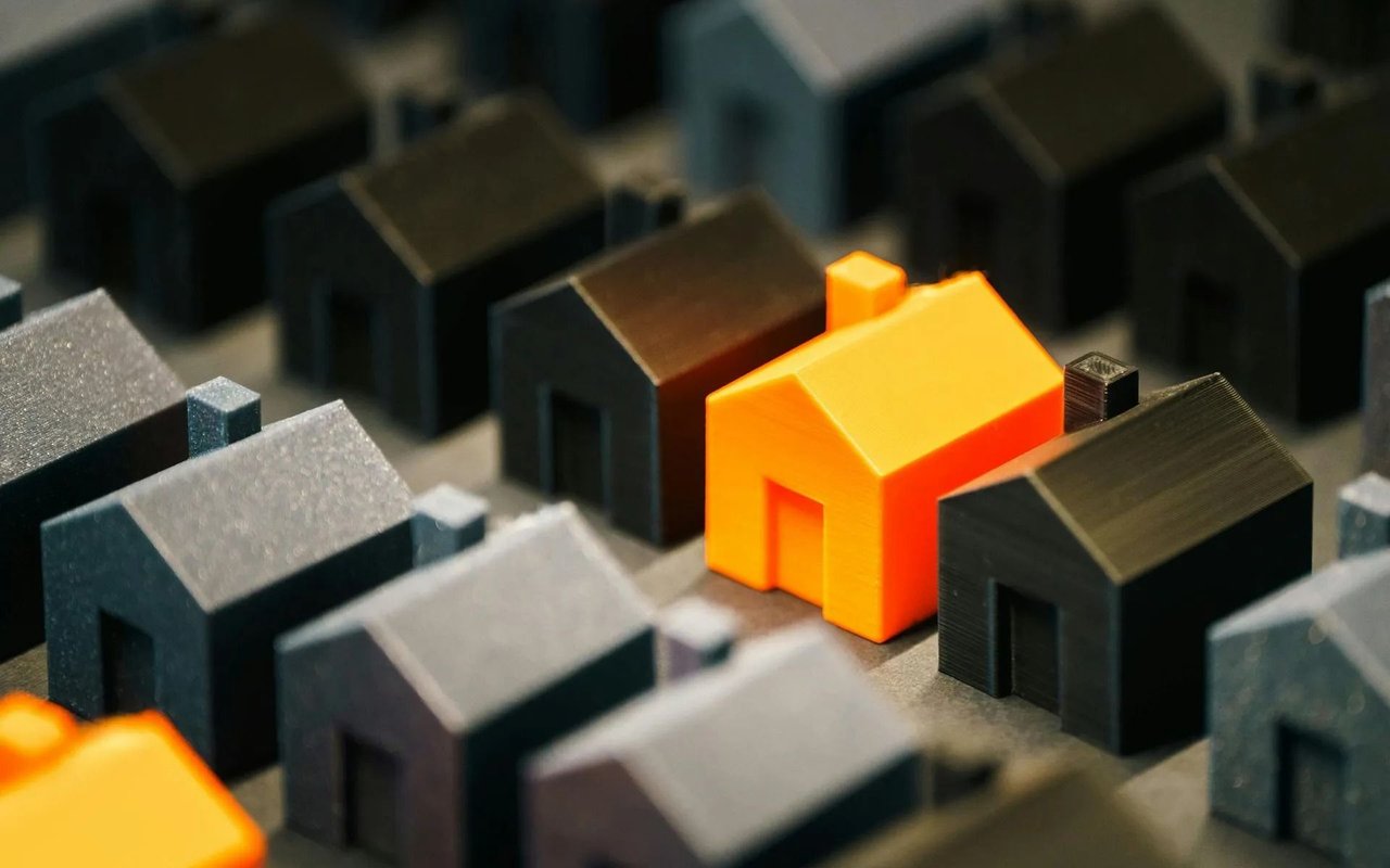 Bright orange miniature house stands out among tightly arranged dark model houses.