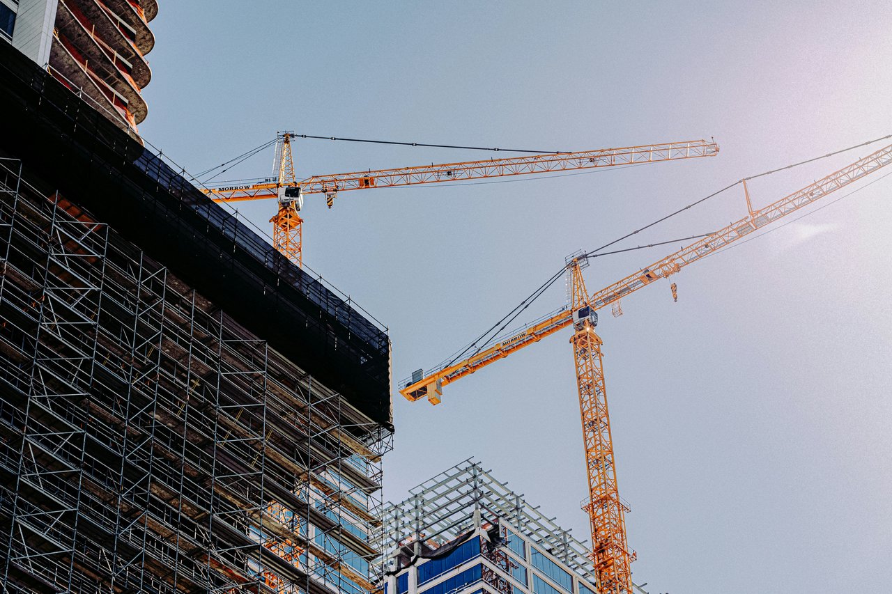 High-rise construction site with scaffolding and orange tower cranes.
