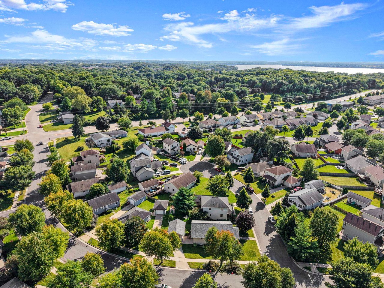 Aerial view of a Madison-area residential neighborhood with homes, mature trees, and a lake in the distance, representing the Dane County housing market in August 2026.