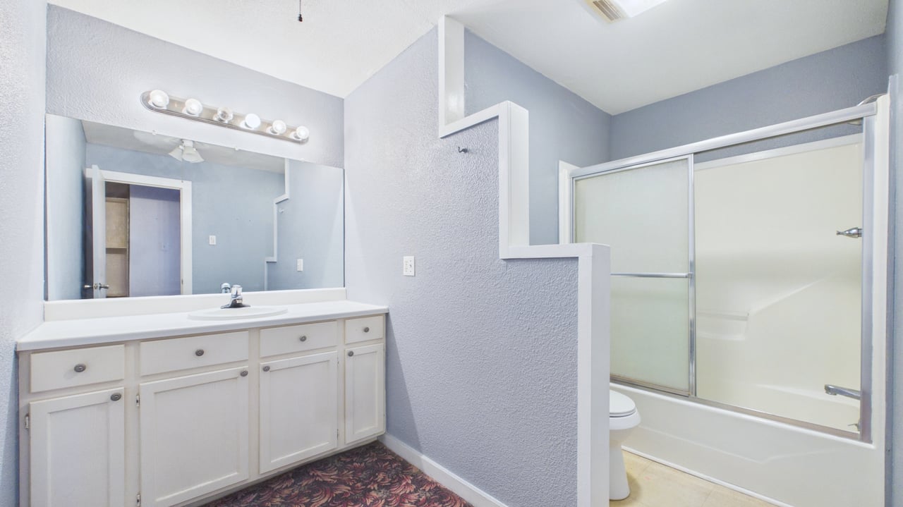 Bathroom with a white vanity, large mirror, and bathtub behind frosted sliding doors.