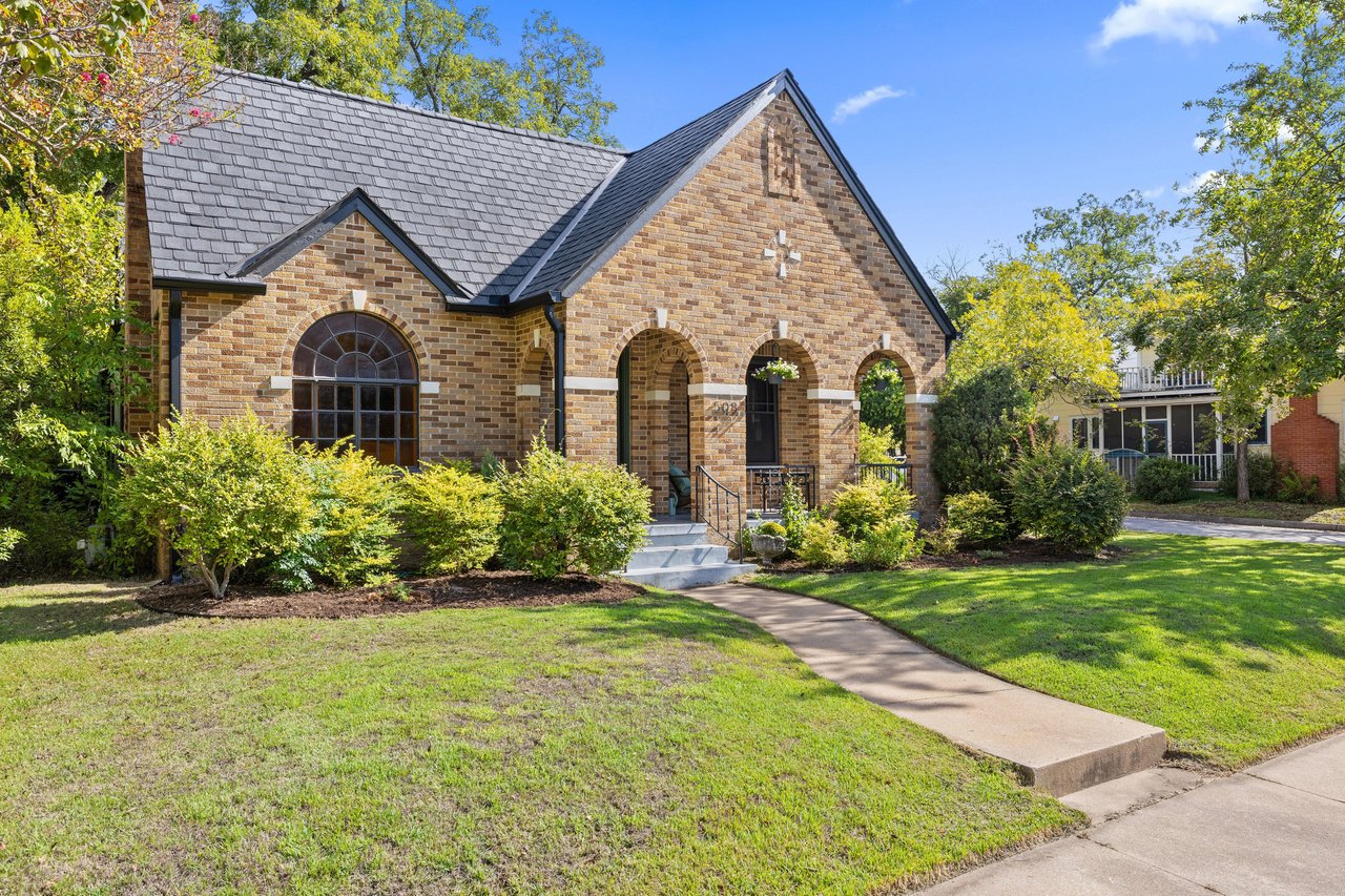 Brick church with arched entryways, a dark slate roof, and a landscaped front lawn.