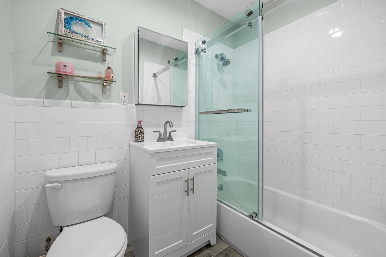 Bathroom with a glass-enclosed tub, white subway tile, and compact vanity.