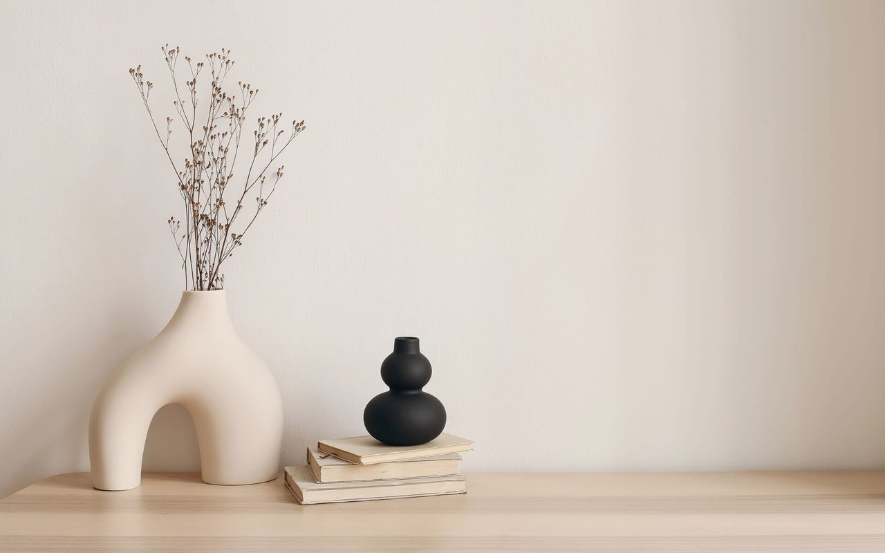 Interior shelf styled with an ivory vase, dried stems, black ceramic vase, and stacked books.