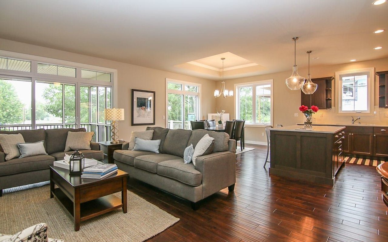 Staged open-plan living room with gray sofas, large windows, and a dark kitchen island.