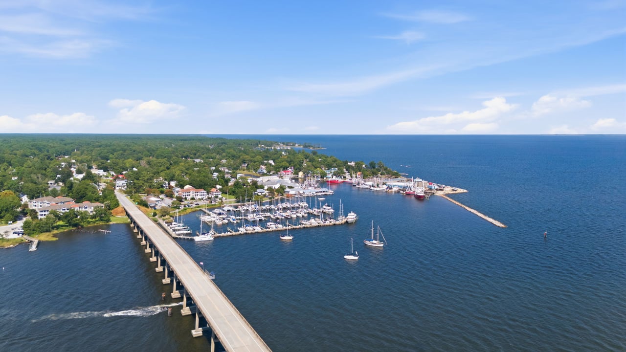 Aerial view of Oriental’s marina and bridge, with sailboats along the wooded waterfront.
