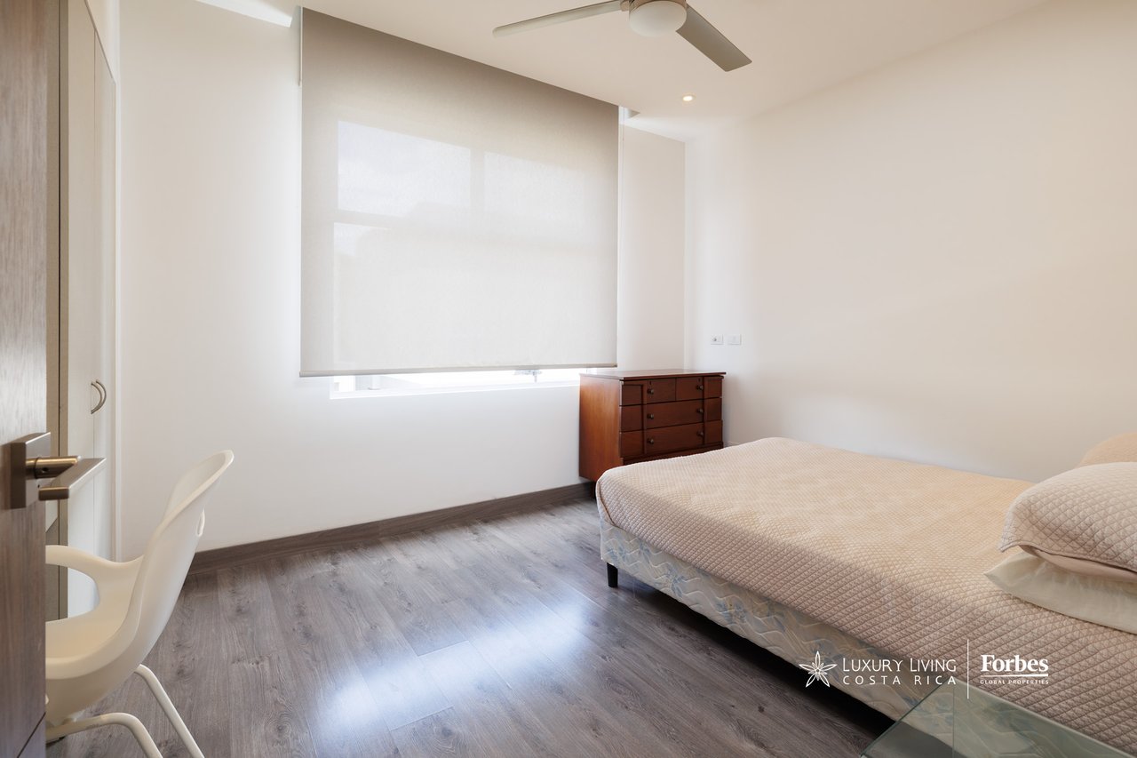 Furnished bedroom with a large bed, gray flooring, and a wide shaded window.