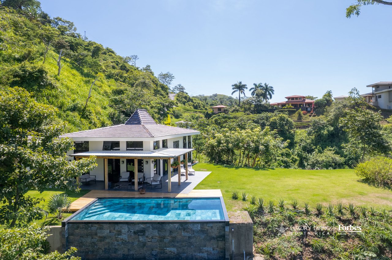 Modern home with an infinity pool and covered patio overlooking a lush valley.