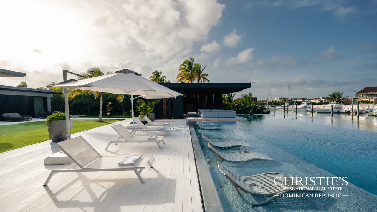 Modern waterfront villa with a pool, white sun deck, and marina beyond.