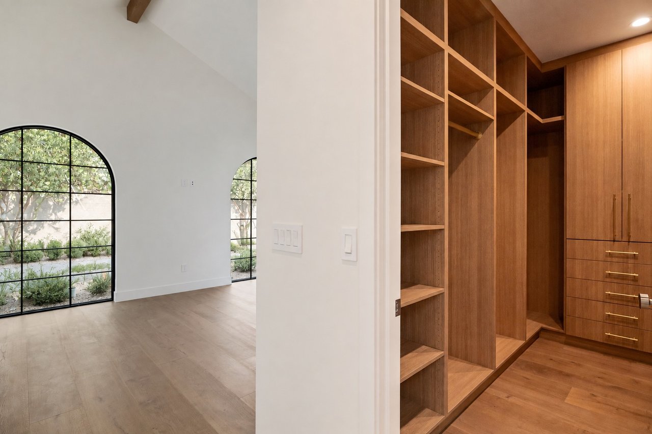 Bright empty room with arched windows beside a spacious walk-in closet with warm wood cabinetry.