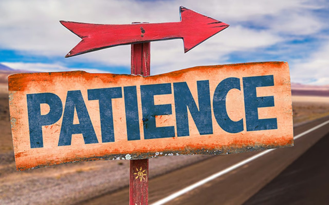 Weathered PATIENCE sign with a red arrow pointing right beside an open road.