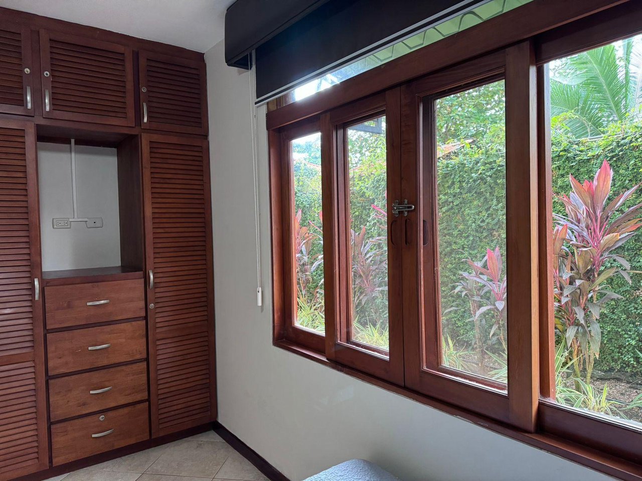 Bedroom with dark wood built-in wardrobes and large windows overlooking tropical greenery.
