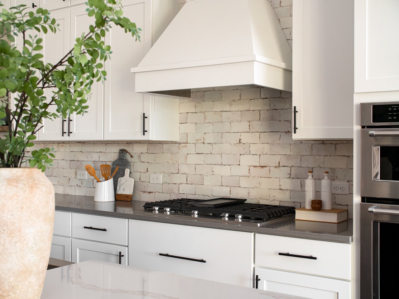 Bright kitchen with white cabinetry, a pale tile backsplash, black gas cooktop, and stainless steel ovens.
