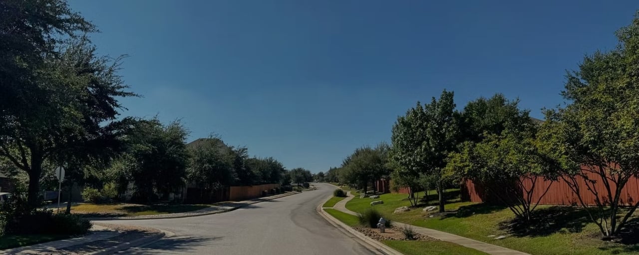 Residential street lined with leafy trees, sidewalks, and red wooden fences.
