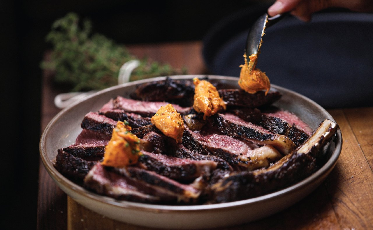 Sliced grilled steak with orange sauce in a shallow bowl.