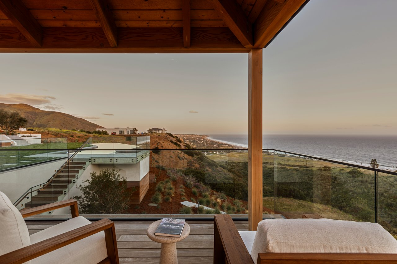 Covered terrace with glass railings, lounge chairs, and a wide view of the Malibu coastline and ocean.