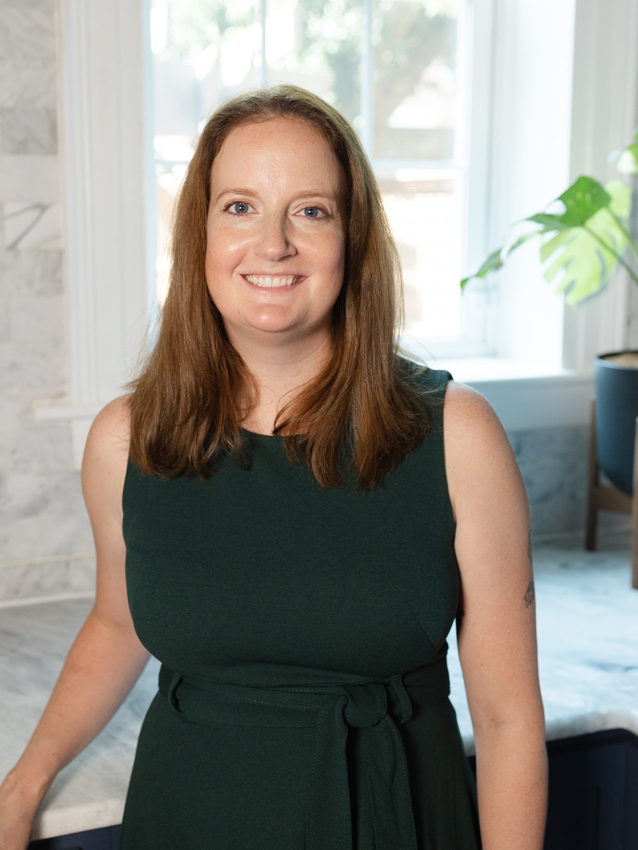 Leigh Bowling smiling in a dark green sleeveless dress indoors.
