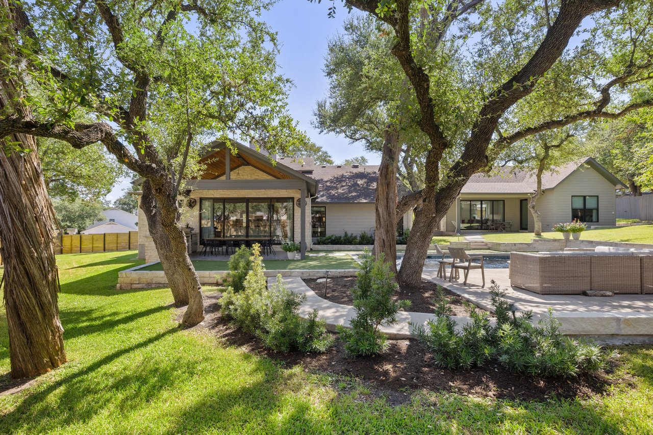 Home’s backyard with covered patio, pool, lawn, and mature oak trees.