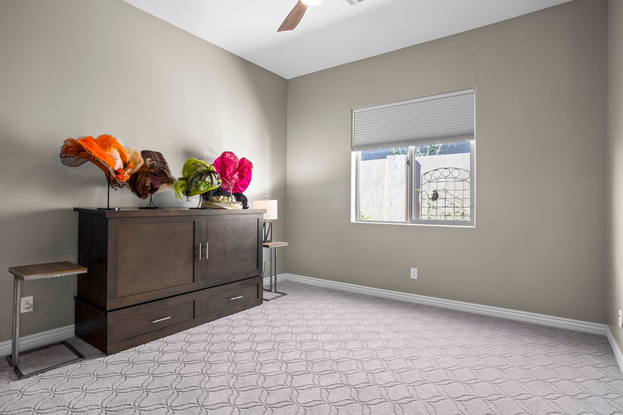 An unfurnished bedroom with a dresser, decorative hats on top, a window with a blind, and carpeted floor.