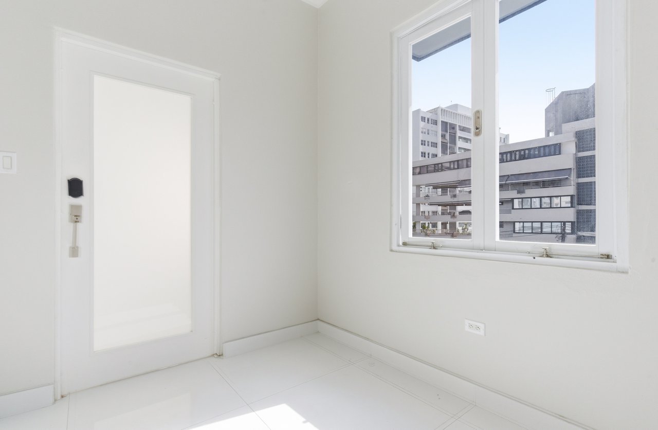Empty white-tiled room with a large window overlooking city buildings.