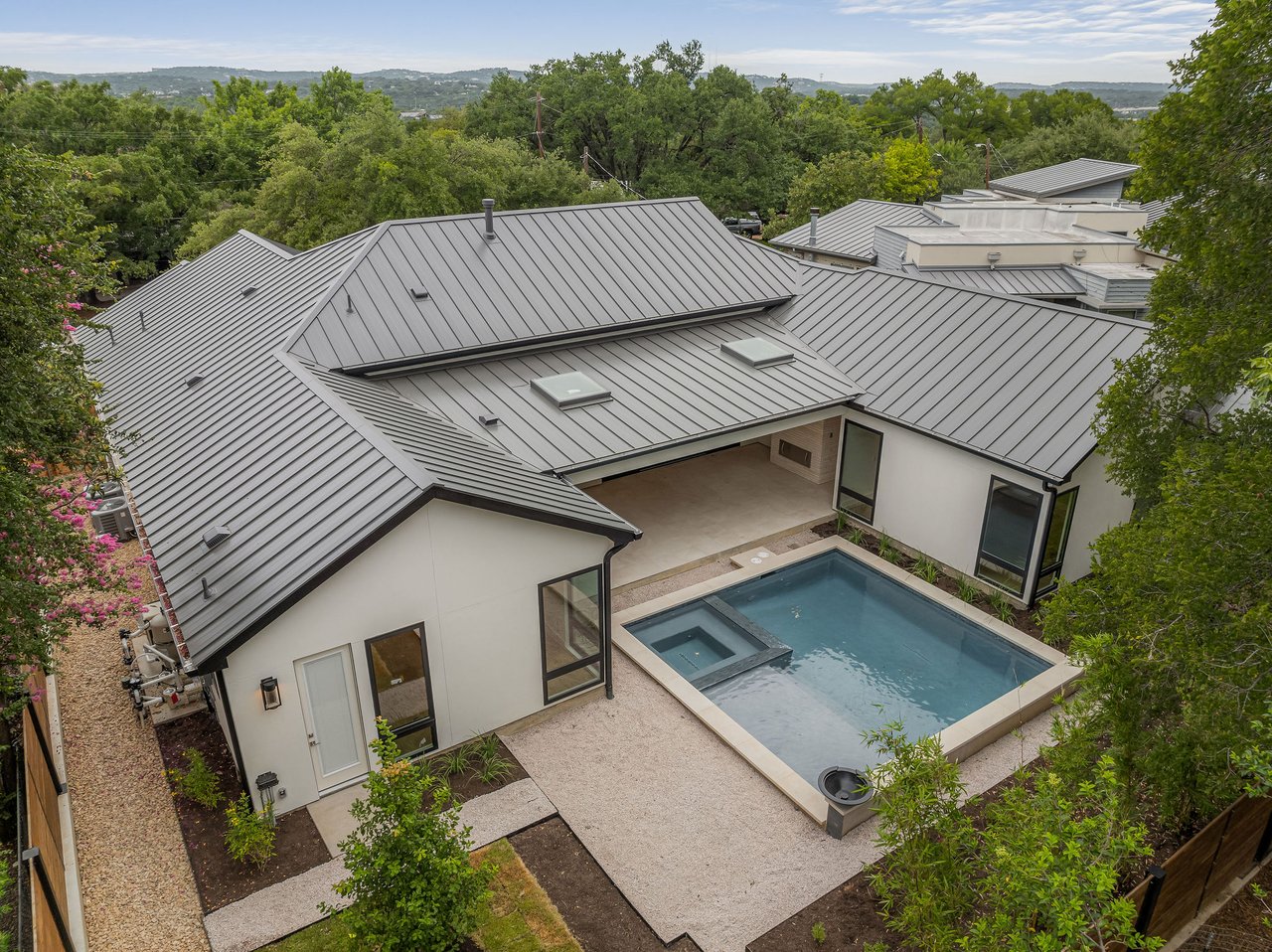 Aerial view of the rear of 1001 Bluebonnet Ln in Zilker, Austin, showing the metal roof, pool and raised spa, covered patio, and mature oak trees. Built by Rivendale Homes.
