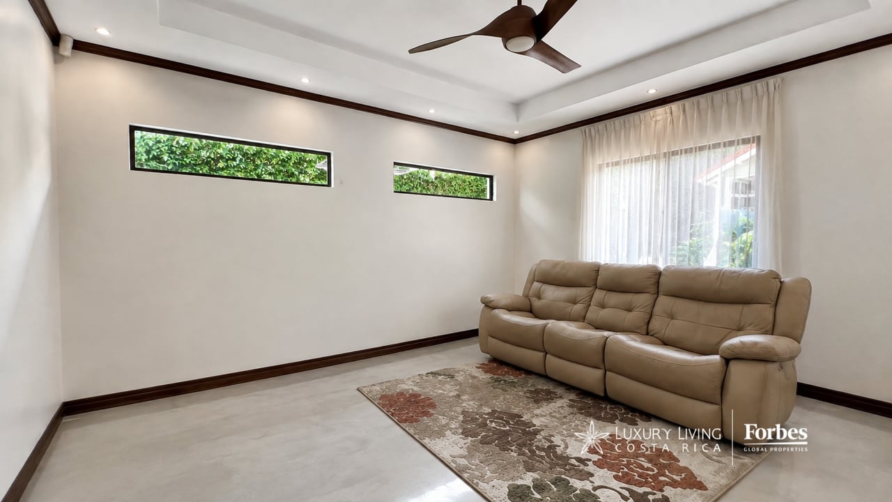 Living room with beige leather sofa, patterned rug, ceiling fan, and narrow high windows.