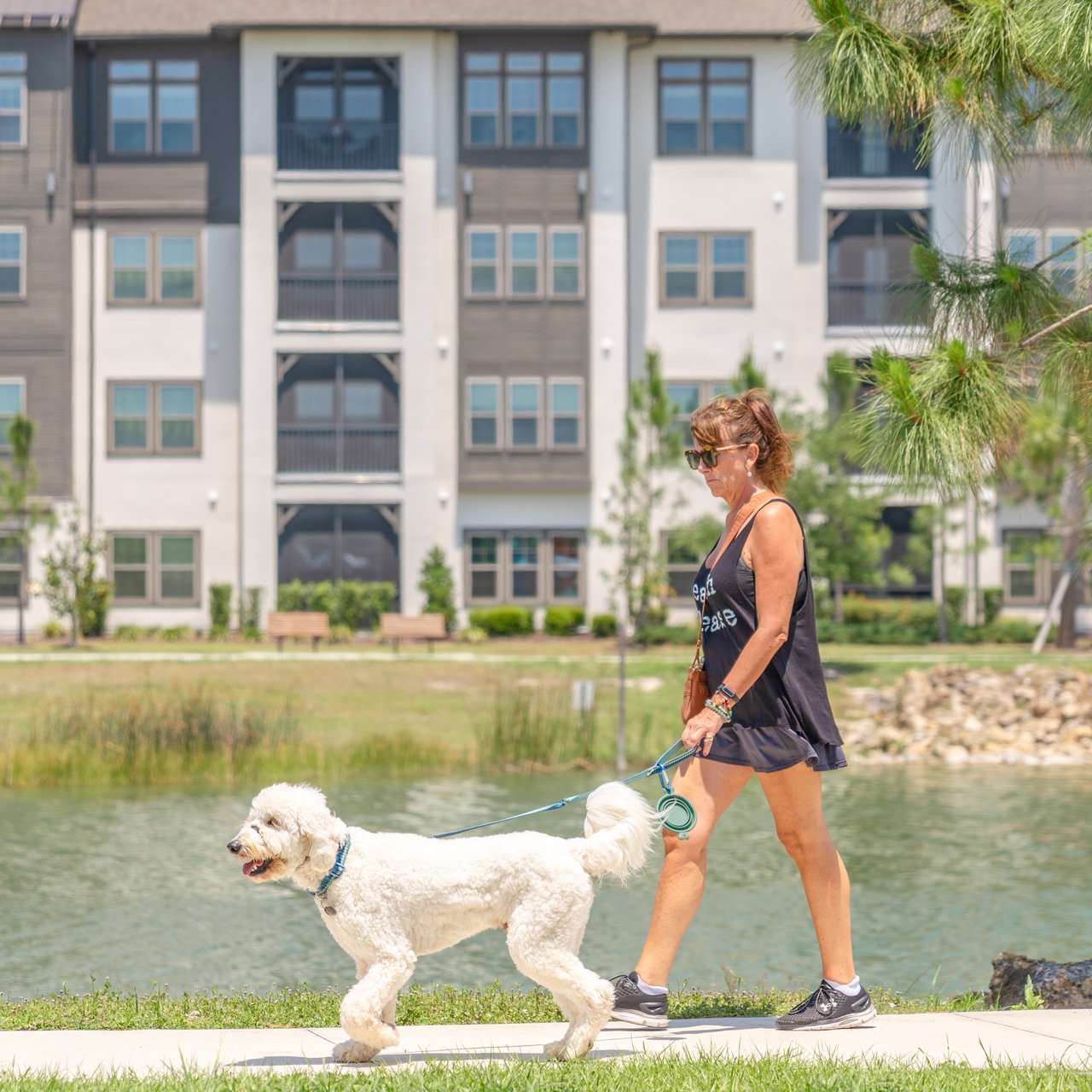 Apartment building beside a pond as a woman walks a fluffy white dog.