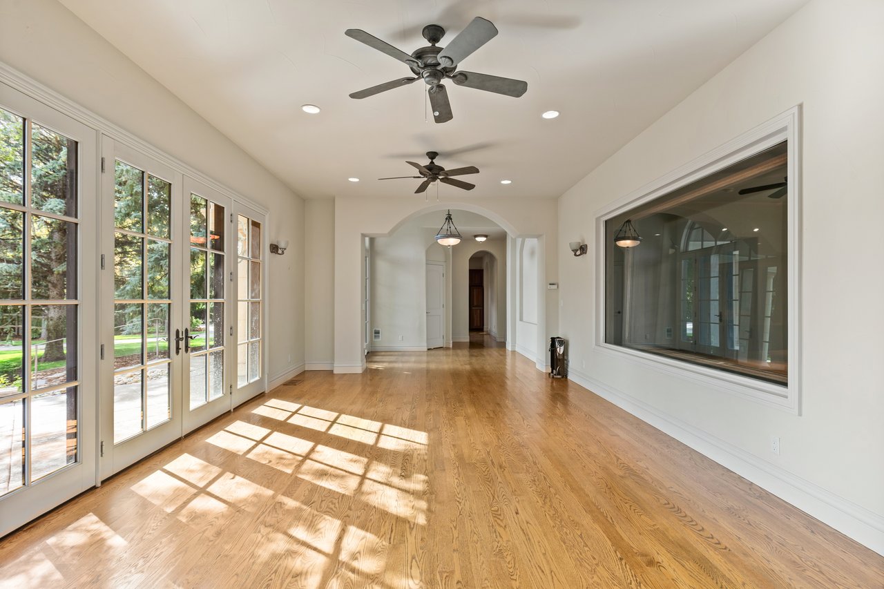 Bright, empty room with hardwood floors, French doors, and two ceiling fans.