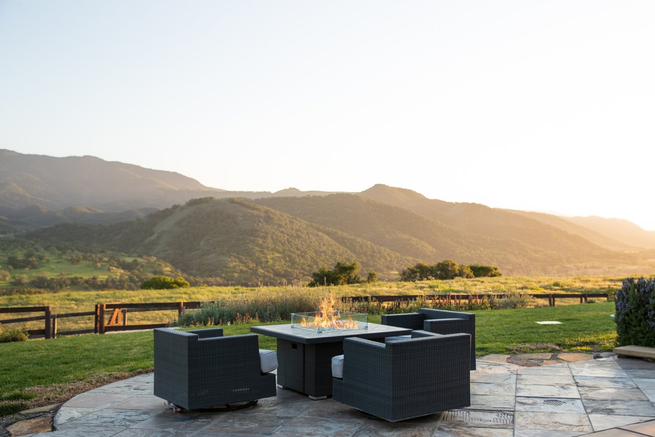 Patio seating around a fire table overlooks rolling mountains at golden hour.