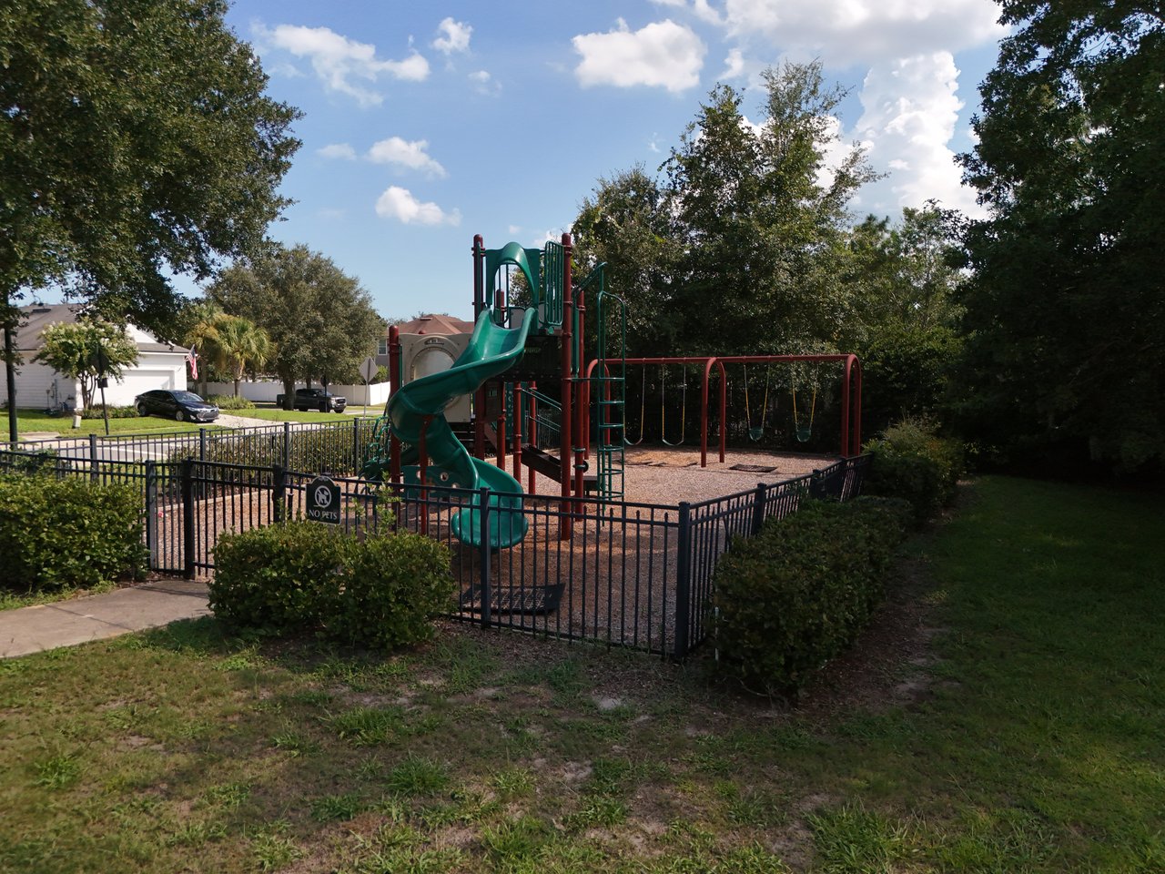 Neighborhood playground with a green spiral slide, swings, and black metal fencing.