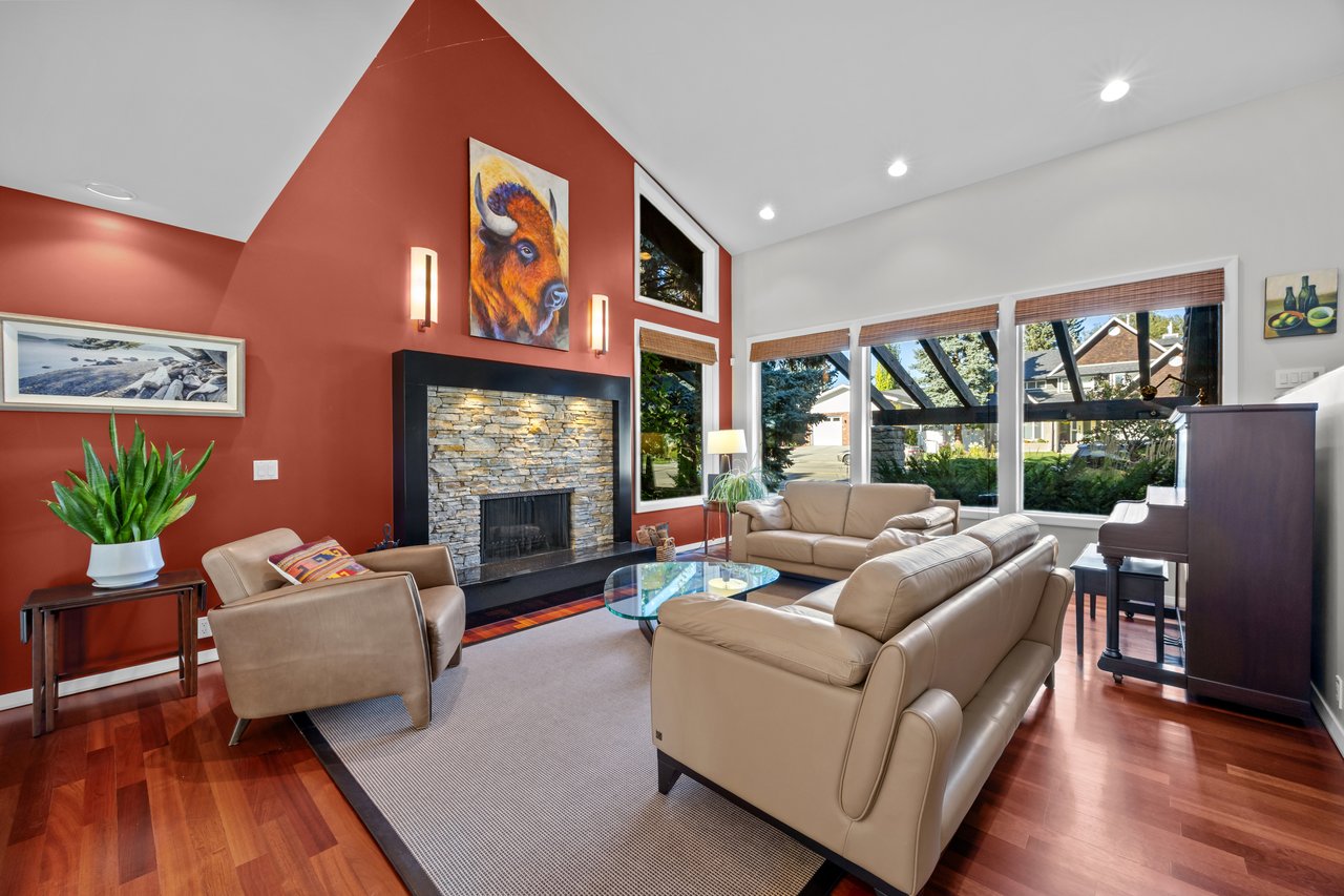 Living room with a tall vaulted ceiling, stone fireplace, rust-red walls, and large windows.