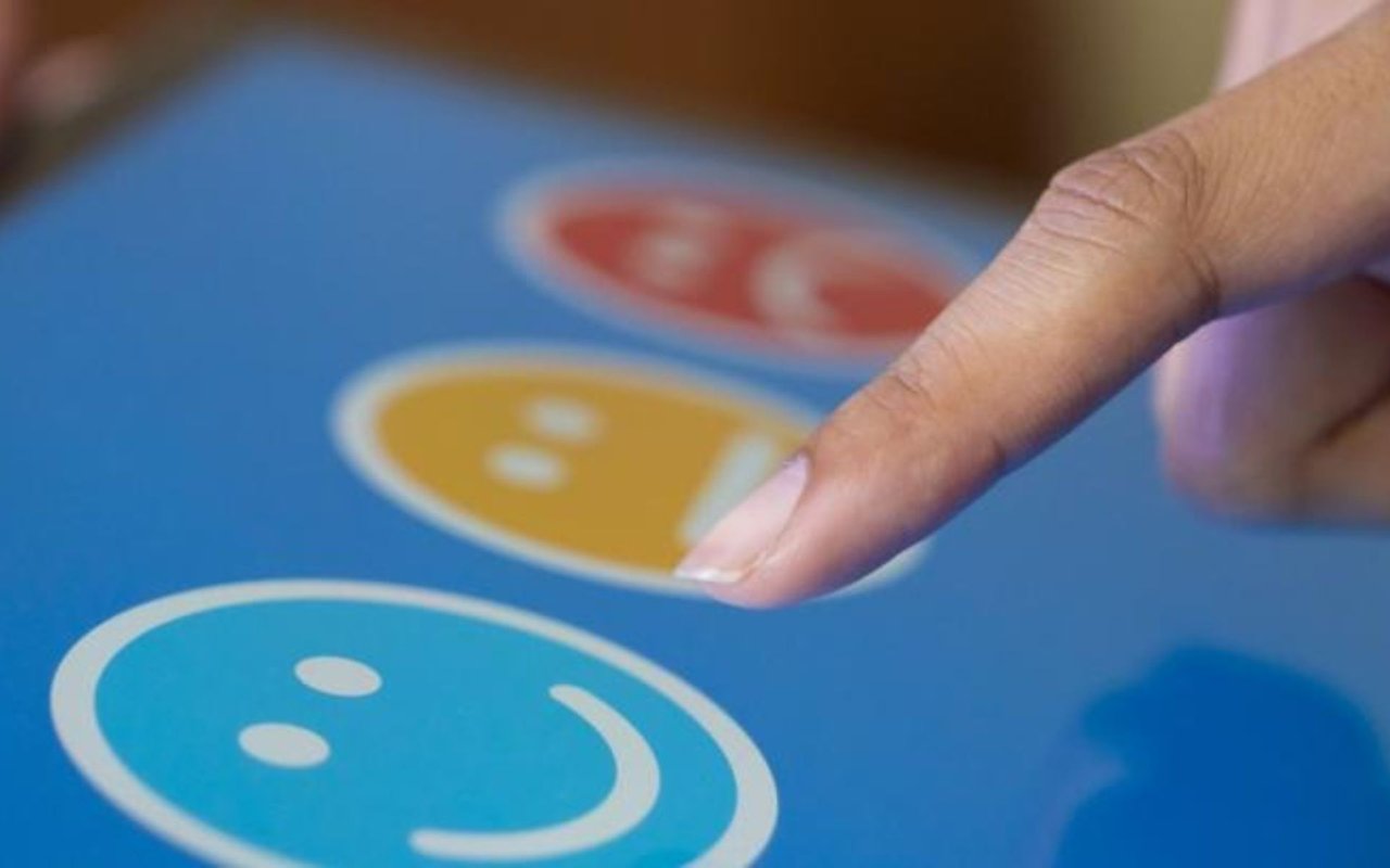 Finger selecting a smiling face on a blue satisfaction-rating screen.