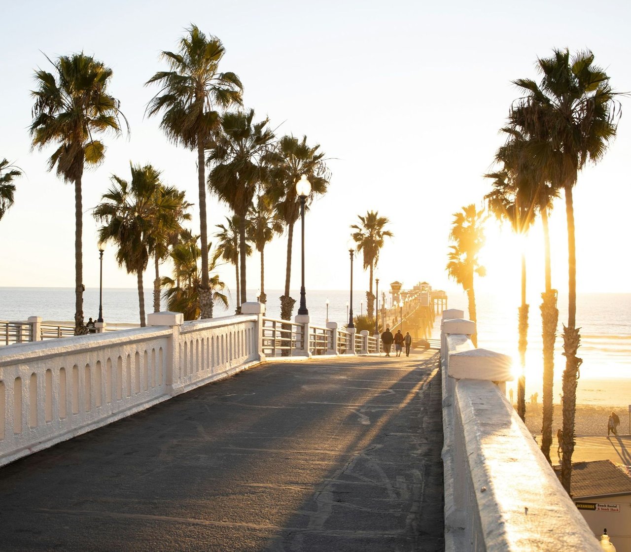 Palm-lined seaside pier and promenade stretching toward the ocean at sunset.