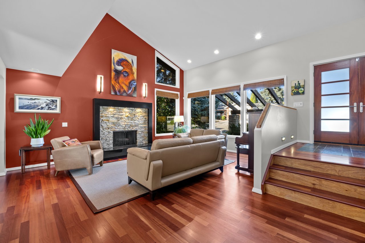 Living room with a stone fireplace, red accent wall, vaulted ceiling, and large windows.