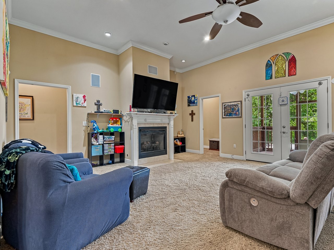 Furnished living room with a fireplace, wall-mounted television, ceiling fan, and French doors.