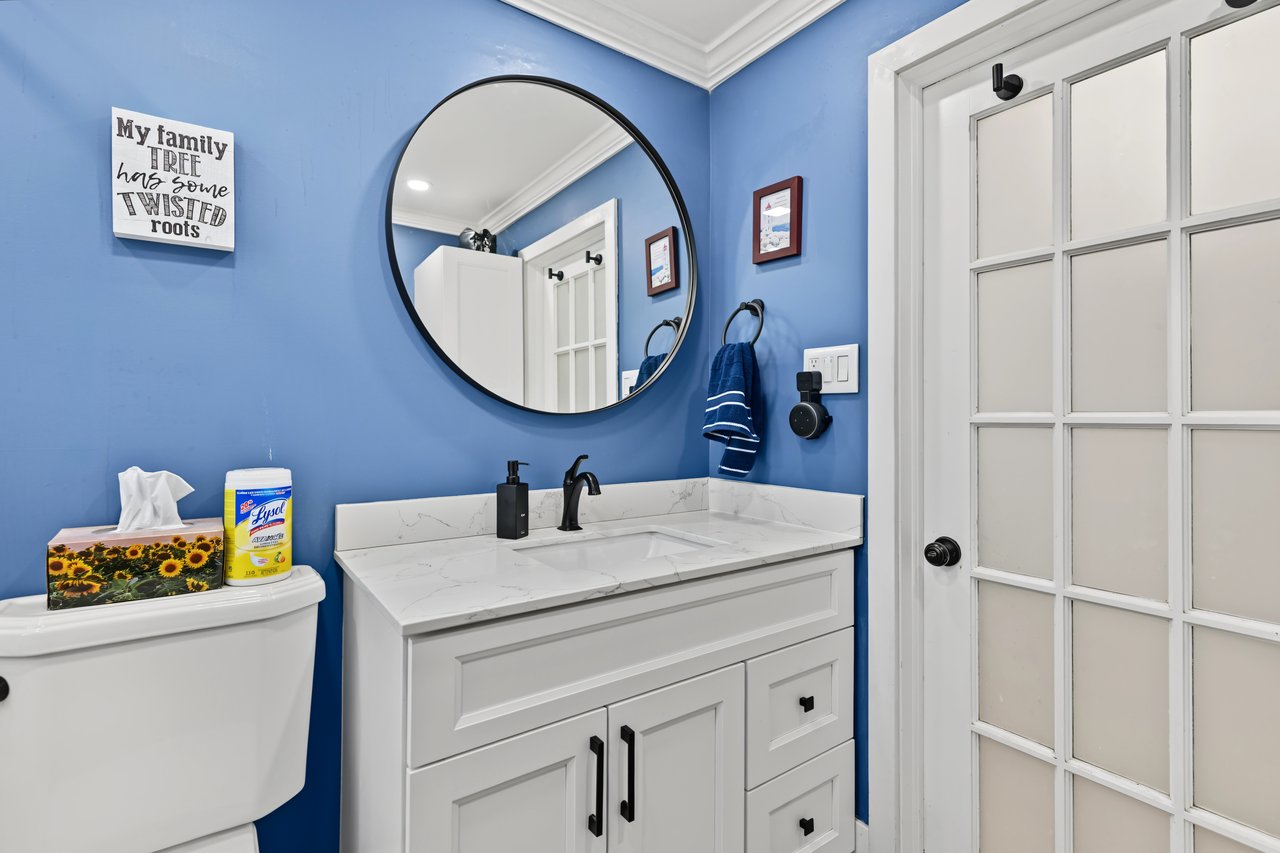 Bathroom with blue walls, white vanity, marble-look countertop, round mirror, and glass-paneled door.