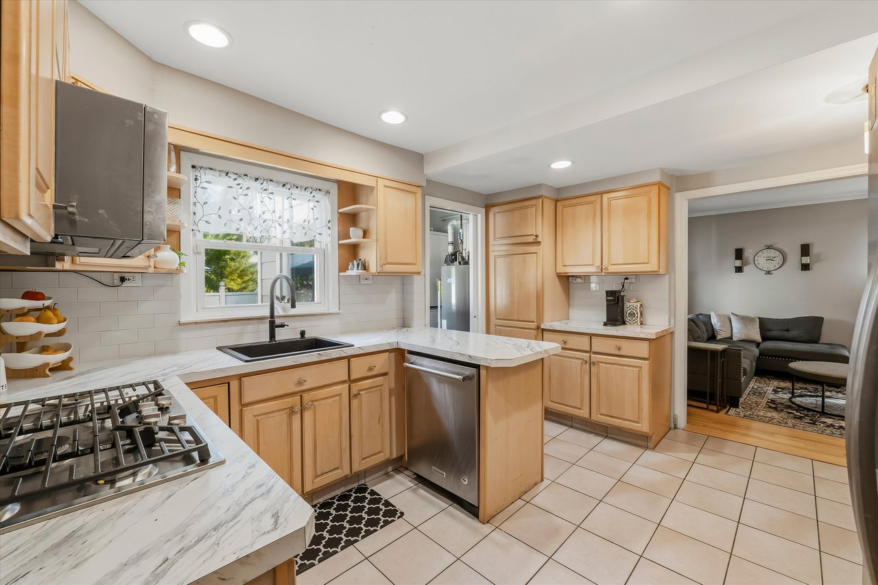Kitchen with honey-toned cabinets, marble-look counters, stainless steel appliances, and an adjoining living room.