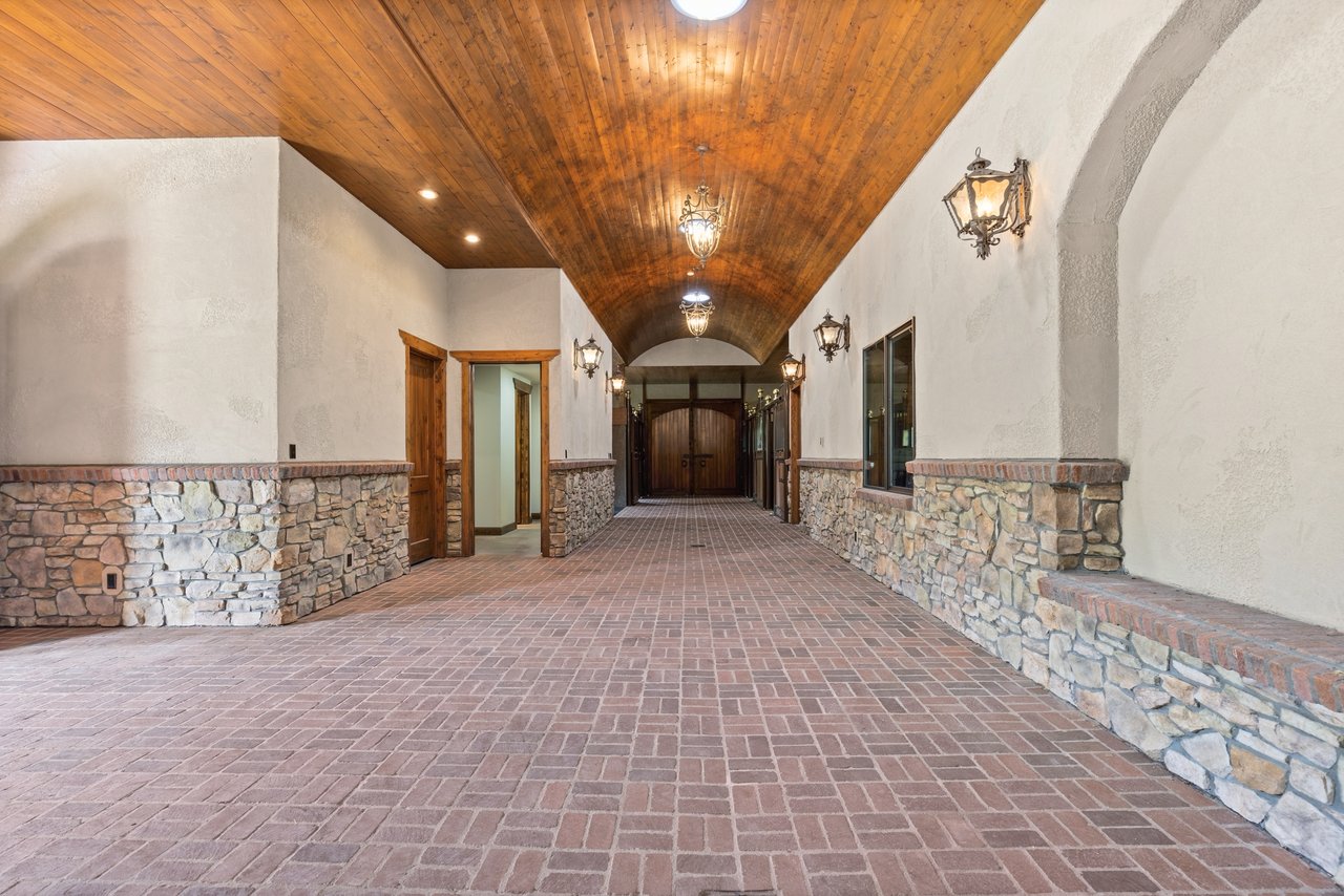 Barn passage with a brick floor, stone half-walls, and a vaulted wood ceiling.