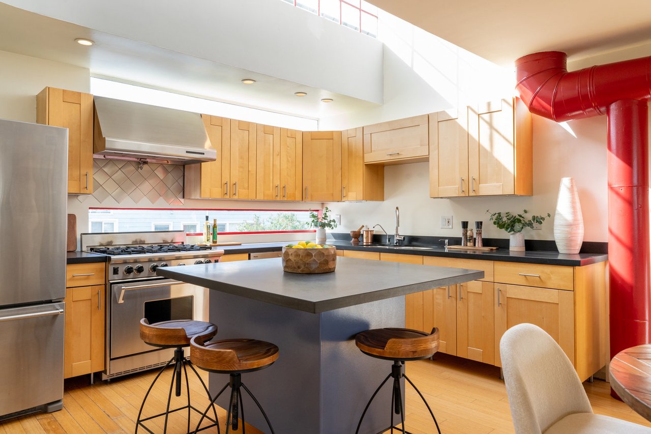 Contemporary kitchen with light wood cabinets, island seating, stainless appliances, and a red exposed duct.