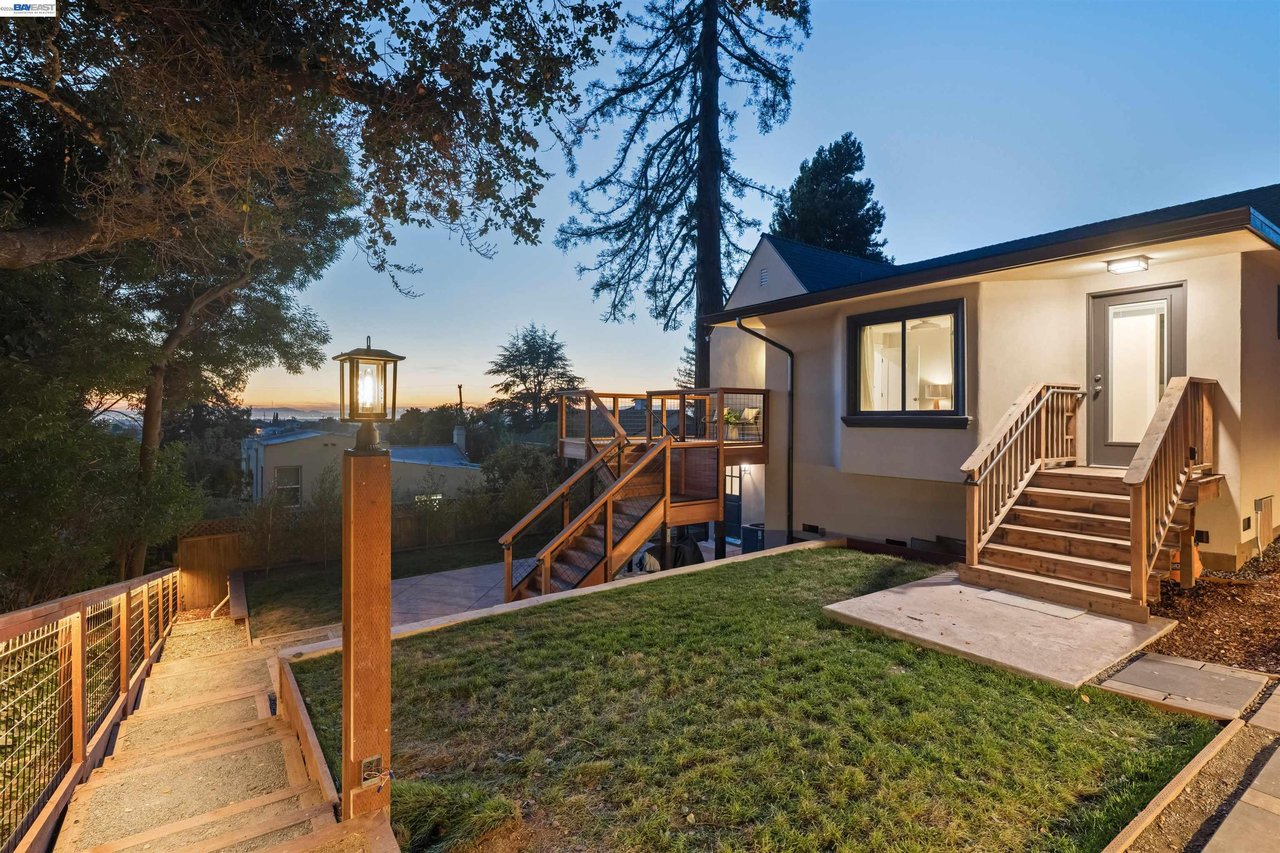 Oakland home at dusk with a raised wooden deck, fenced yard, and illuminated path lamp.