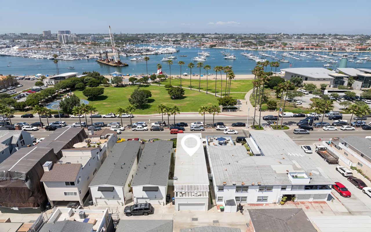 An aerial view of a coastal city with a white pin marking a house, with a park and marina filled with boats in the background.