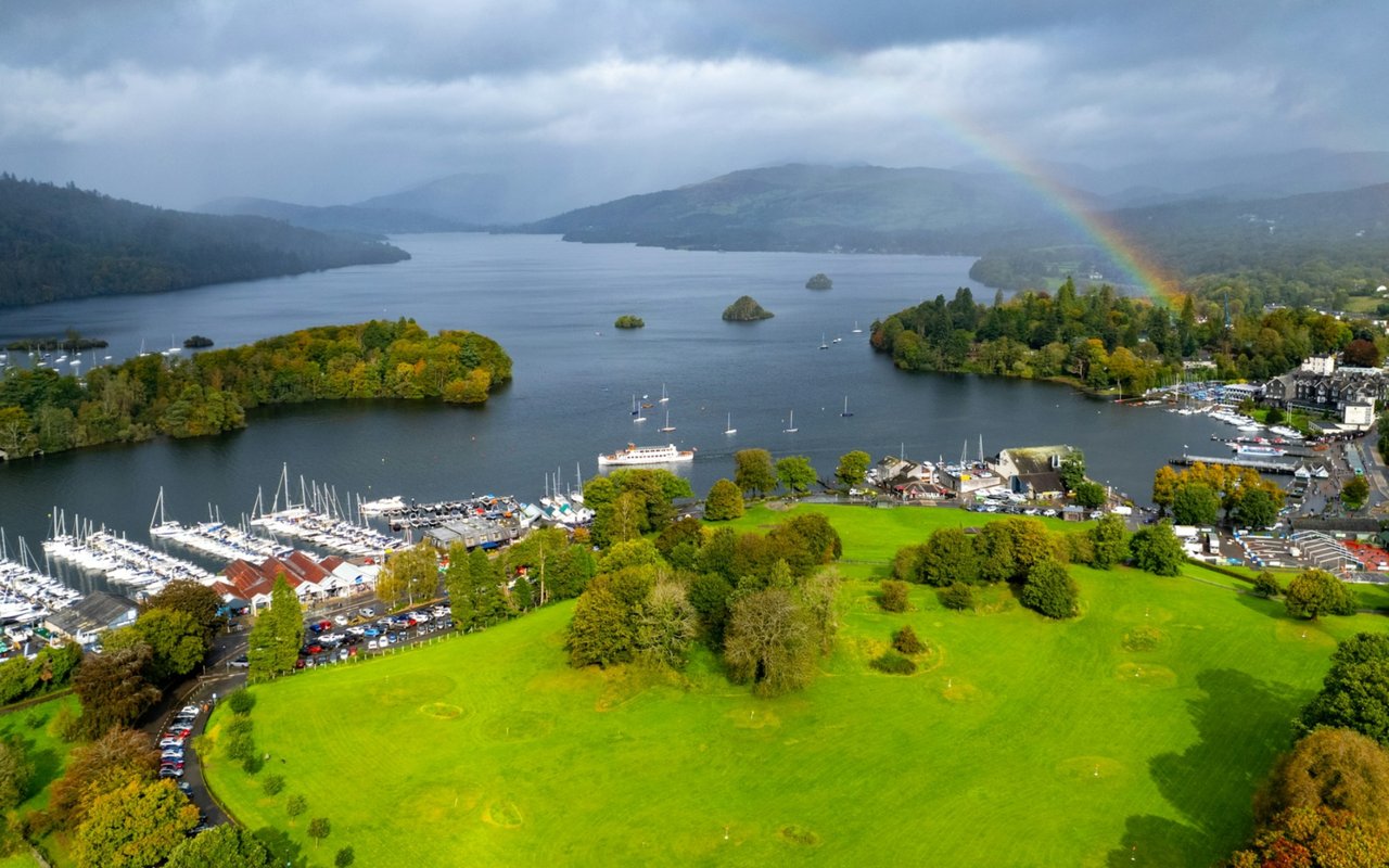 Aerial lake view with marinas, wooded islands, green parkland, and a rainbow.