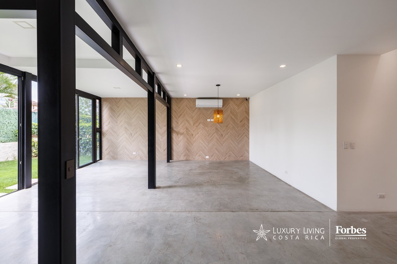 Vacant open-plan living and dining room with concrete floors, black steel beams, and a herringbone accent wall.