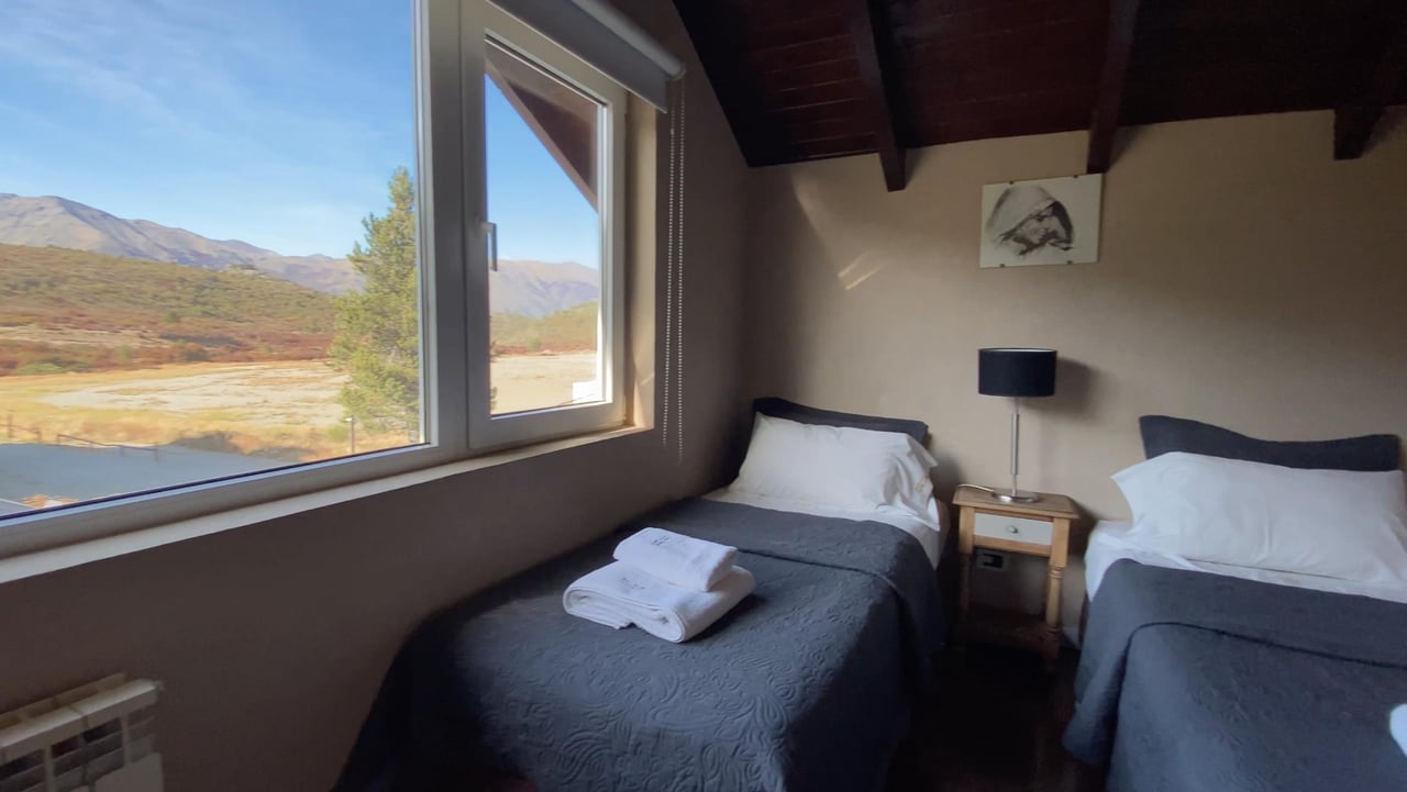 Twin bedroom with folded towels on the beds and large windows overlooking an autumn valley and mountains.
