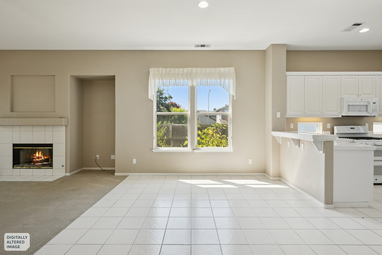 Open living area with tiled flooring, a lit fireplace, and an adjoining white kitchen.