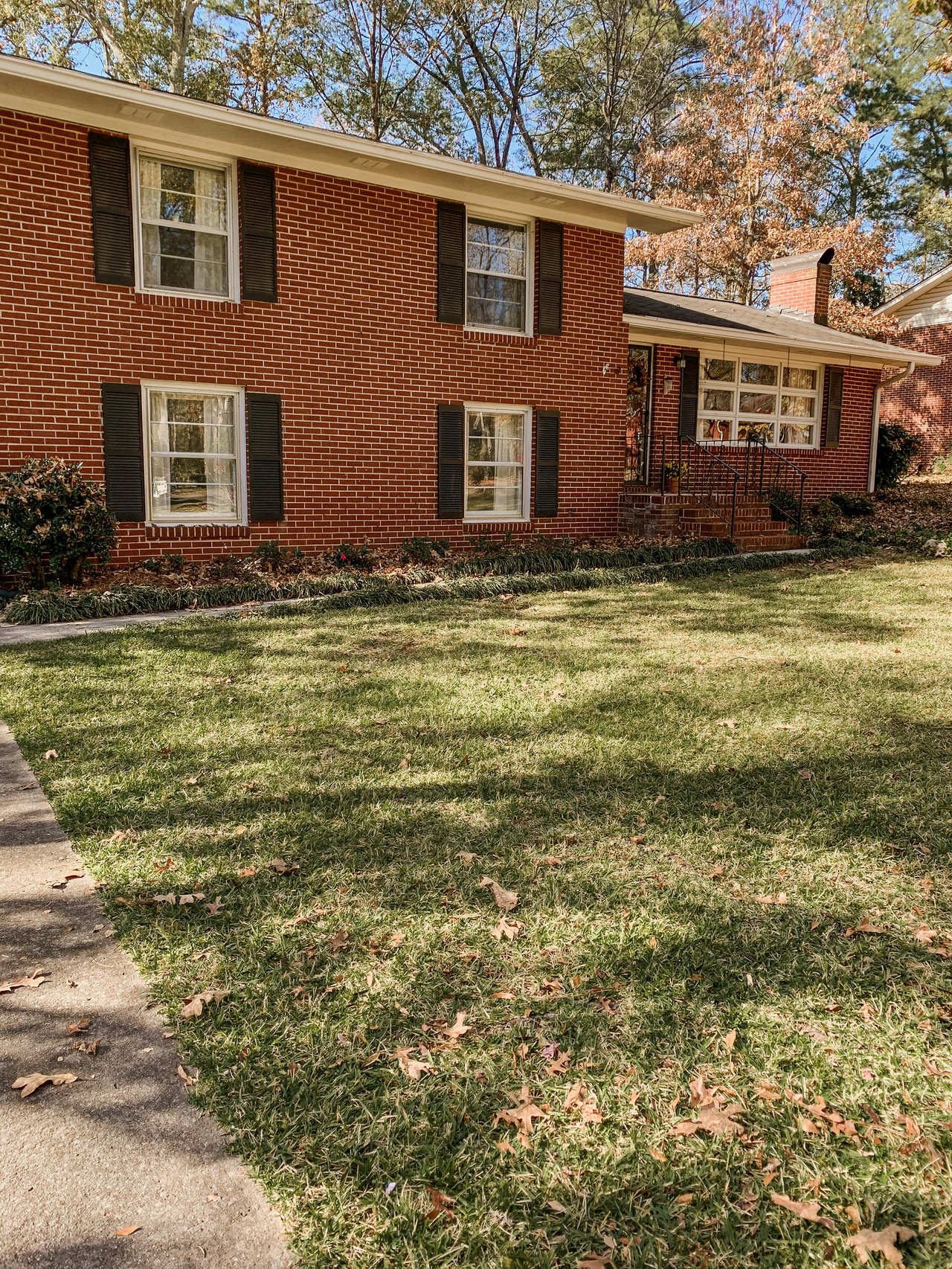 Red-brick split-level house with black shutters, a covered entry, and a broad front lawn.