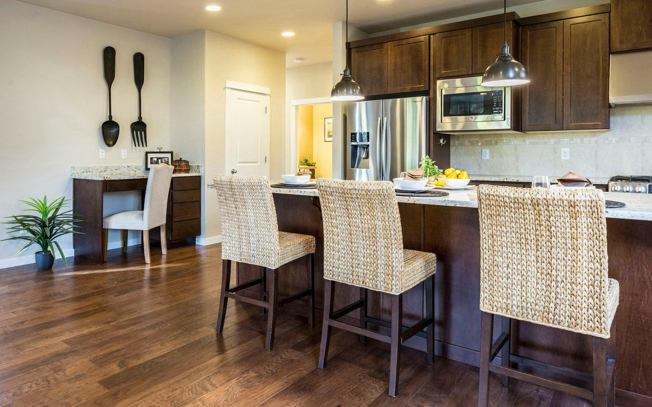 Kitchen with dark wood cabinets, stainless steel appliances, and a granite island with woven bar stools.
