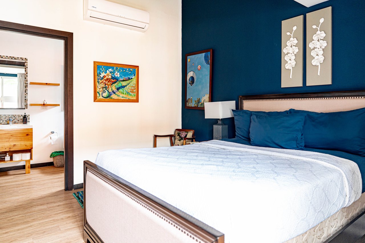 Furnished bedroom with a large bed, deep blue accent wall, and adjoining bathroom.