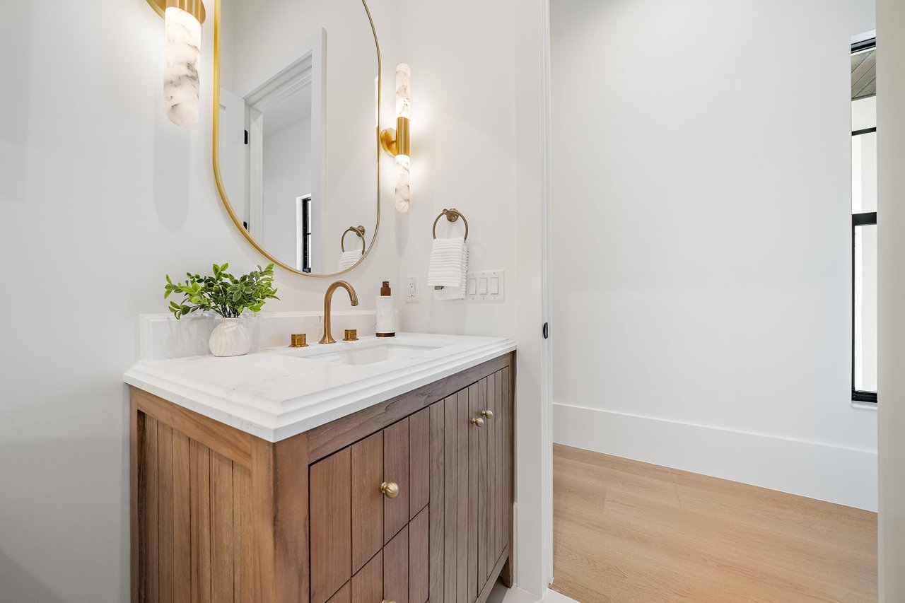 Bathroom vanity with a fluted wood cabinet, white stone counter, brass fixtures, and oval mirror.