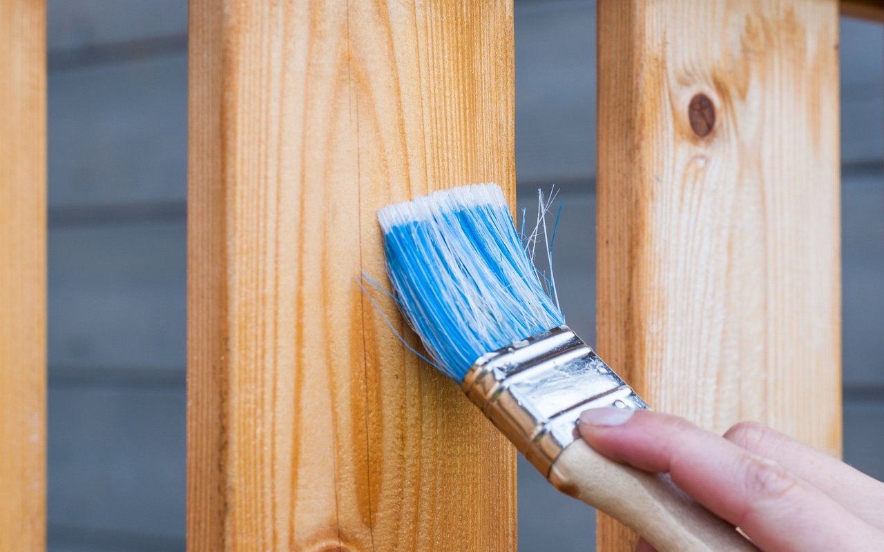 A hand brushes paint onto a wooden fence.