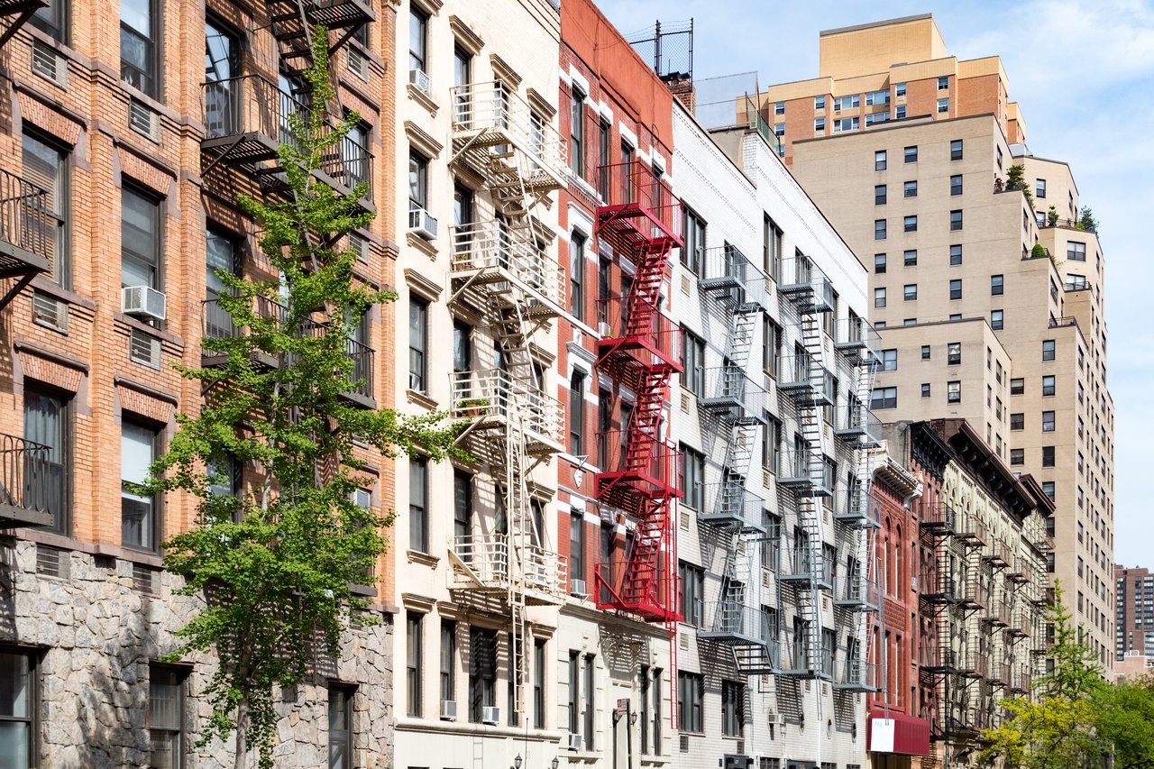 Urban residential buildings with rows of windows and fire escapes, including a prominent red fire escape.